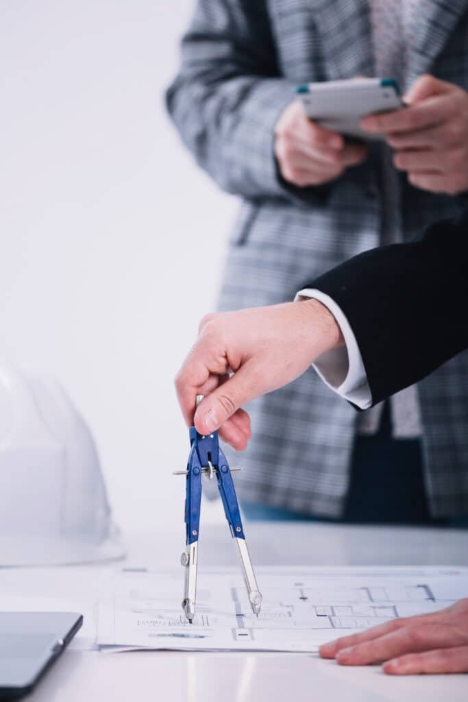 Main tenant un compas au-dessus de plans architecturaux, symbolisant la conception de tiny houses.
